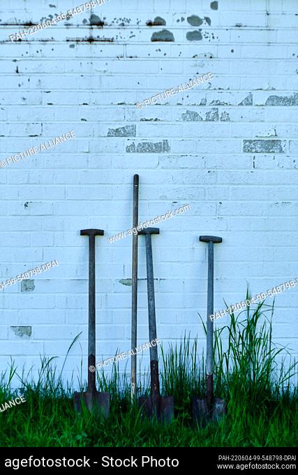 09 May 2022, Lower Saxony, Brunswick: Garden tools stand against a white wall next to the burial hall at the cemetery in the Watenbüttel district