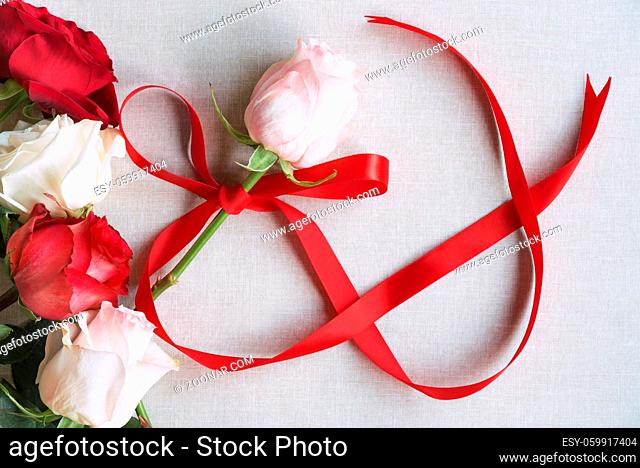 Women day image with a pink rose tied with a red ribbon in shape of the number 8, surrounded by red and white roses, on a vintage fabric background