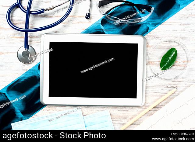 Flat lay workplace of doctor in modern clinic. Tablet computer with blank screen, x-ray image, stethoscope and cardiogram lies on wooden desk