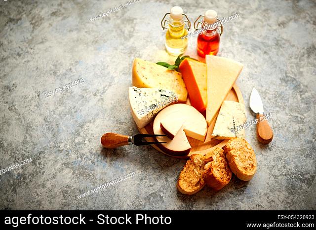 Various types of cheese served on rustic wooden board. Placed on concrete background