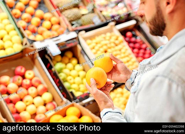 Over shoulder view of bearded man standing at food counter and buying citrus fruits to strengthen immunity at market
