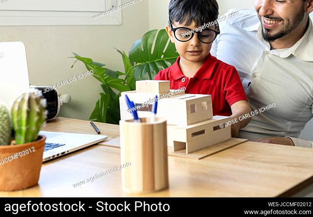 Boy with eyeglasses looking at house model while sitting with father at home