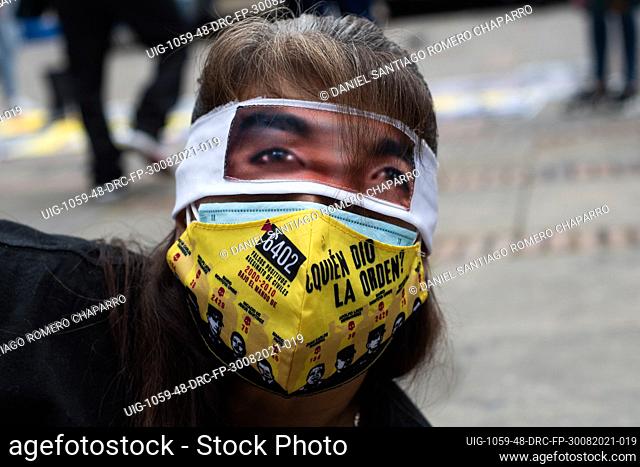 A women lays on the ground wearing a face mask of ""Who gave the order"" with images of army and police generals involved as she covers her eyes with a picture...