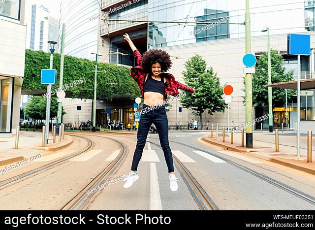 Cheerful woman with arms outstretched jumping on tracks in city