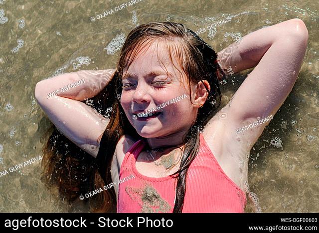 Girl lying on back with hands behind head in water during sunny day