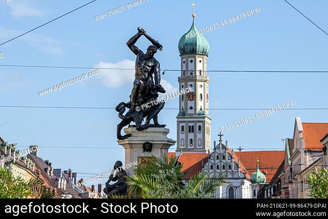 21 June 2021, Bavaria, Augsburg: The fountain statue of Hercules stands in Maximilianstraße in front of the Basilica of St. Ulrich and Afra