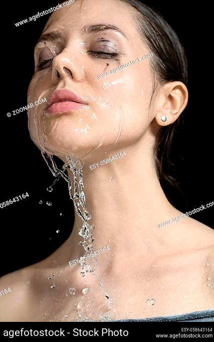 Charming wet girl with closed eyes and parted lips on the black background in the studio. Water flows from her face. Closeup. Vertical