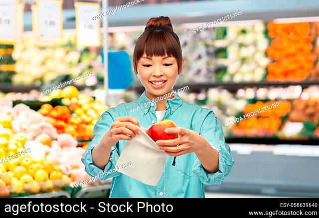 happy woman putting apple into reusable bag