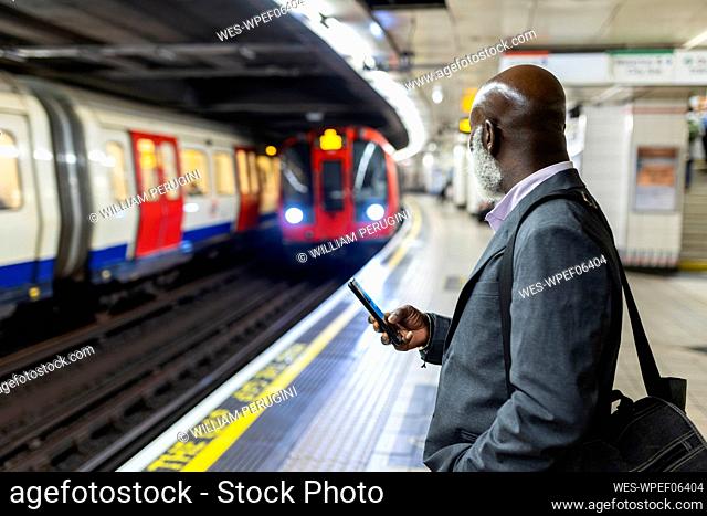 Businessman with smart phone looking at subway train arriving at station