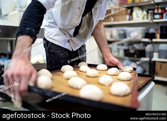 Close-up of baker holding tray with bread rolls in bakery