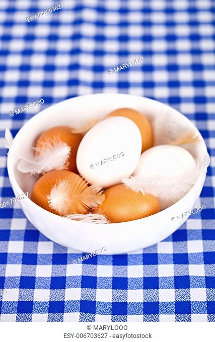 brown and white eggs, feathers in a bowl on tablecloth background