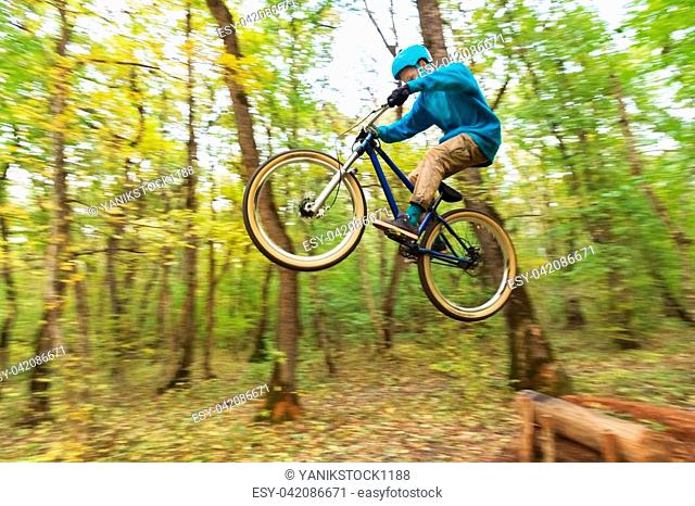 a young rider in a helmet and a blue sweatshirt flies on a bicycle after jumping from a high kicker on a forest bike path
