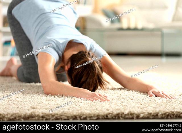 Female exercising yoga melting heart pose on a carpet in the living room at home