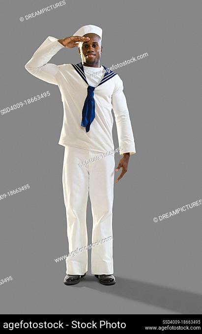 Portrait of a Black man dressed in a sailor Halloween costume looking at camera saluting, on gray background