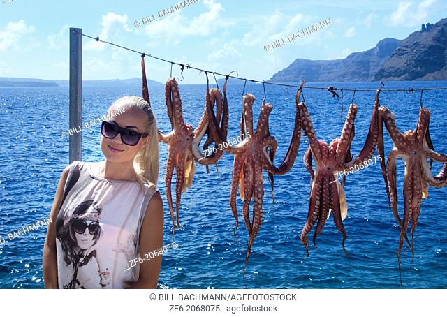 Greece Santorini Oia Cyclades Greek Islands fishing village with Europen woman tourist below Oia with octapus squid hanging on rope Greek; Islands; beautiful;...