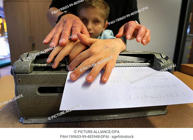 01 June 2019, Bavaria, Würzburg: The deaf-blind Lucas, supported by his educator Stefanie Tröster, feels for letters in Braille which he had typed into a...