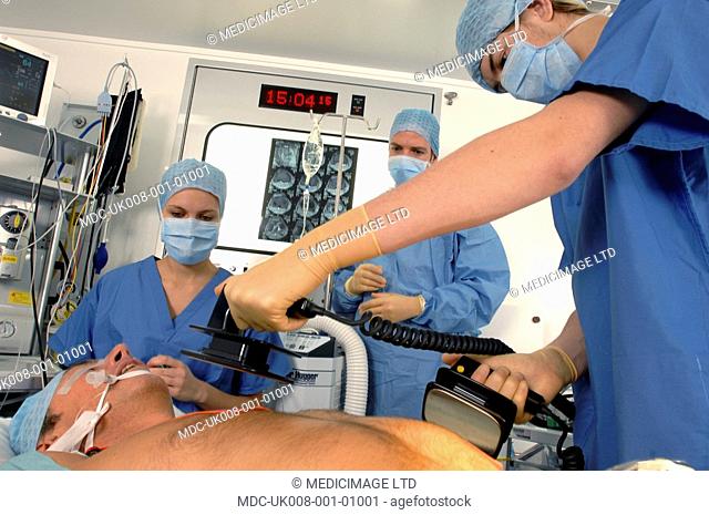 Doctors using a defibrillator to resuscitate a male heart attack victim