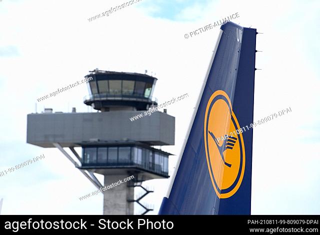 10 August 2021, Brandenburg, Schšnefeld: The logo on the tail unit of a Lufthansa aircraft can be seen against the backdrop of the tower at Berlin Brandenburg...