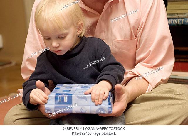 40 year old father holds his 2 year old son as the child opens a Channuka present