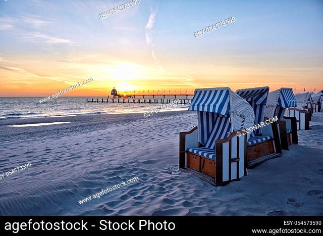Strand am Ostseebad Zingst mit den typischen Strandkoerben und der Seebruecke mit Tauchglocke im Hintergrund, menschenleer bei Sonnenaufgang