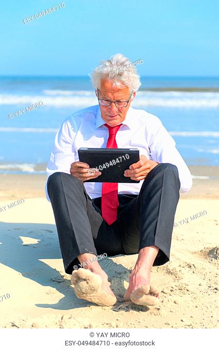 Business man in formal suit sitting and working with tablet at the beach