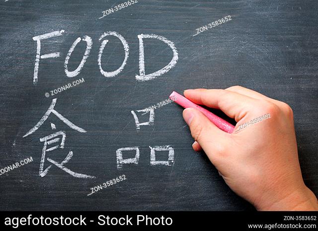 Food - word written on a smudged blackboard with a Chinese translation, with a hand holding chalk