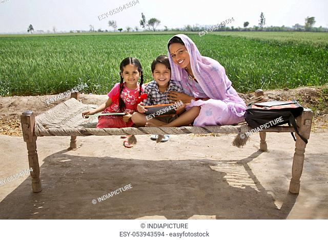 Portrait of a happy mother sitting with her kids on cot