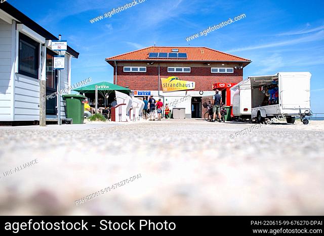 15 June 2022, Lower Saxony, Hooksiel: Several sales booths and beach chairs stand in front of the beach house on the North Sea beach in sunny weather