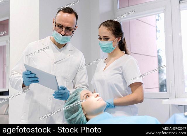 Young woman getting dental treatment in clinic, denist and assistant using digital tablet
