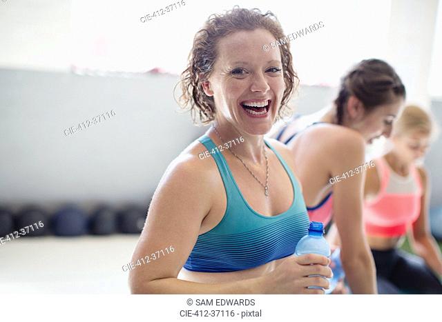 Portrait smiling, laughing woman drinking water and resting post workout at gym