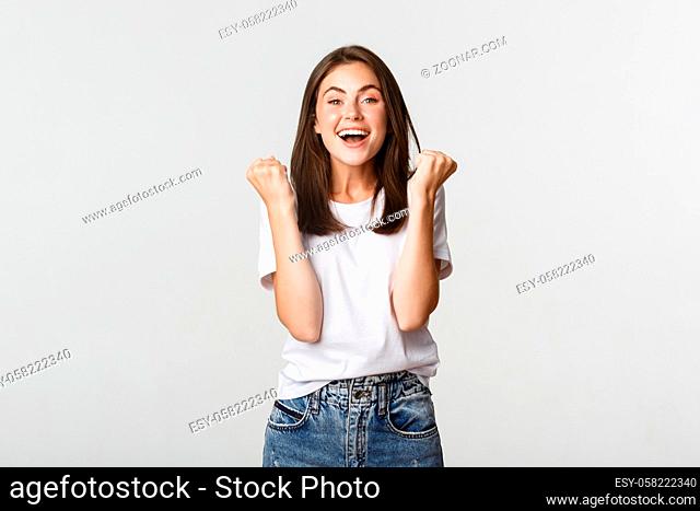 Cheerful attractive brunette girl fist pump and smiling with rejoice, winning