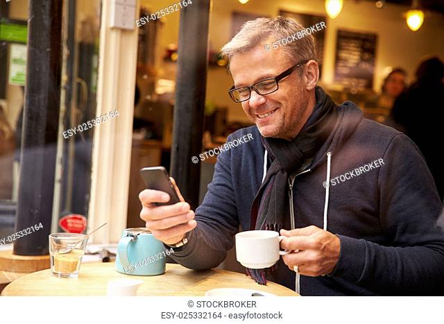 Man Viewed Through Window Of Café Using Mobile Phone