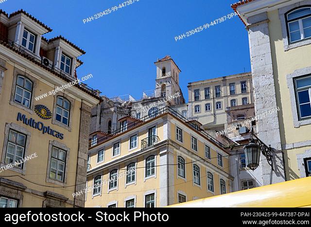 PRODUCTION - 05 April 2023, Portugal, Lissabon: The logo of the company ""Multiopticas"" hangs on one of the yellow-painted house facades on ""Praça Dom Pedro...