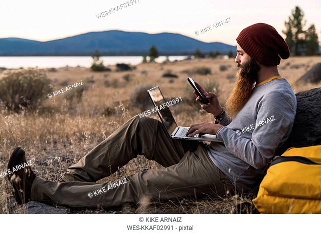USA, North California, bearded young man using cell phone and laptop near Lassen Volcanic National Park