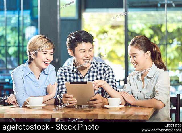 Group of smiling friends looking at digital tablet with coffee cups on table in the cafe