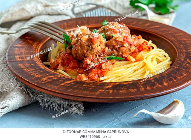 Meatballs in tomato sauce with parmesan and spaghetti in a brown ceramic plate