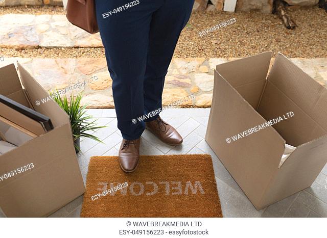 Low section of man with cardboard boxes standing on welcome mat in front of door at home