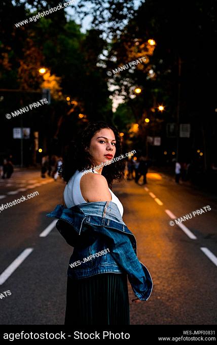 Beautiful woman wearing denim jacket while standing on street at sunset