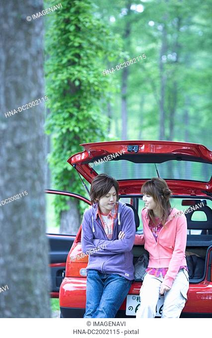 Young Couple Sitting on Vehicle Trunk and Chatting