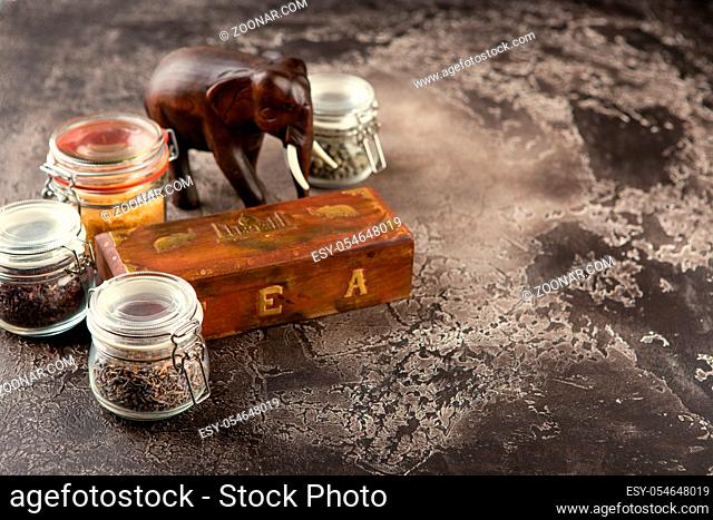 Different kinds of tea in glass jars, wooden box with tea and figurine of a wooden elephant
