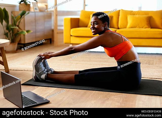 Happy young woman practicing stretching exercise at home