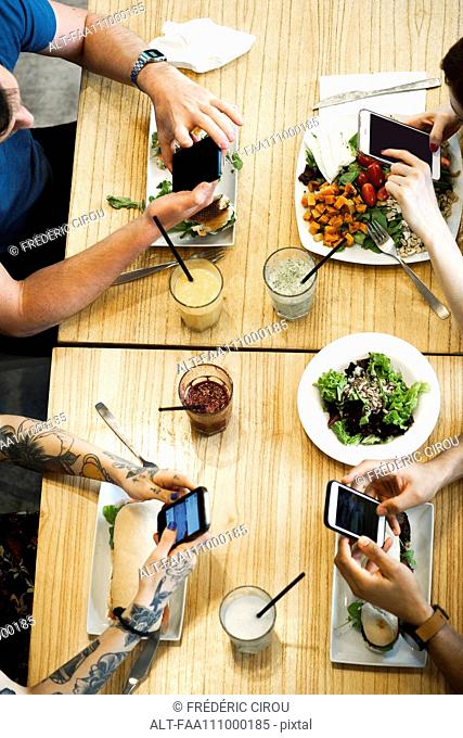 Diners using smartphones in restaurant, cropped overhead view