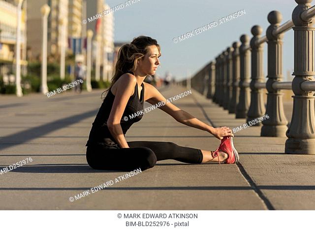 Caucasian teenage girl sitting on boardwalk stretching legs