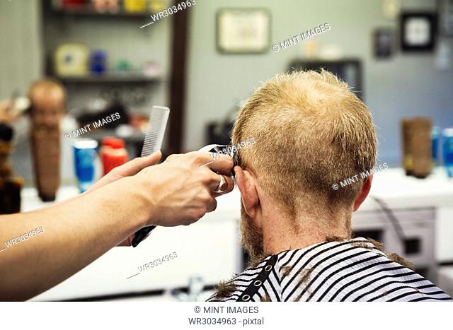 A customer sitting in the barber's chair, and a barber using an electric shaver to shave his head