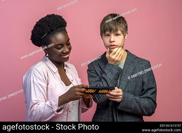 Reflection. Smiling dark-skinned woman looking at abacus in hands and caucasian guy with down syndrome thinking touching his chin