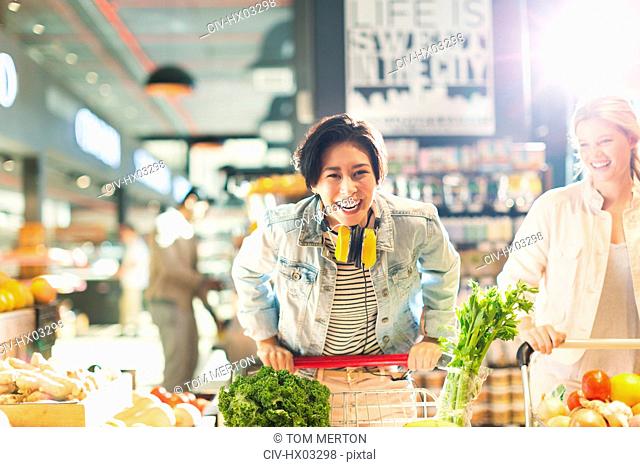 Portrait playful young woman with shopping cart grocery shopping in market