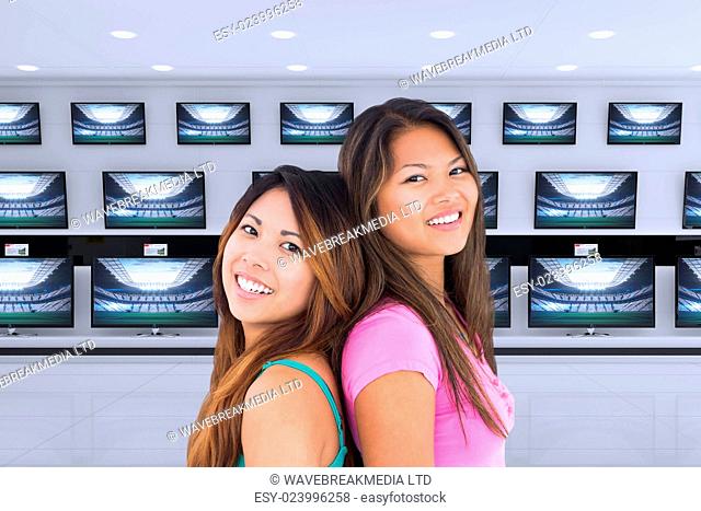 Two beautiful girls posing for the camera against televisions for sale