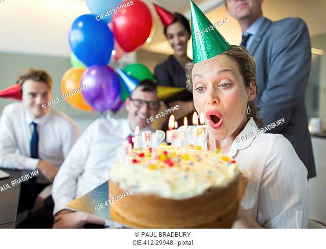 Colleagues watching businesswoman blowing out birthday cake candles