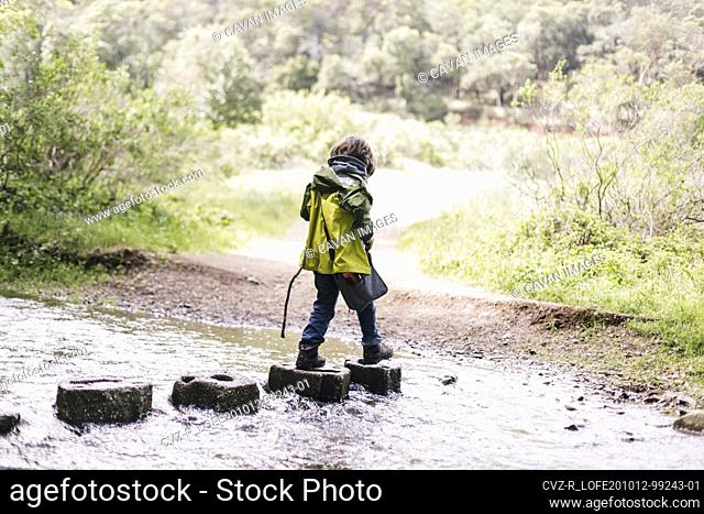 Hiking kid wearing raincoat crossing a river