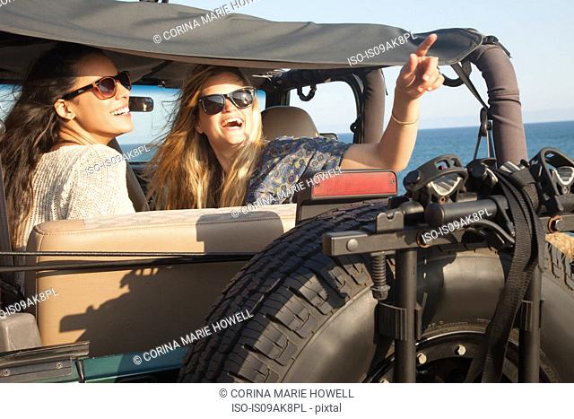 Two young women looking up from jeep at coast, Malibu, California, USA
